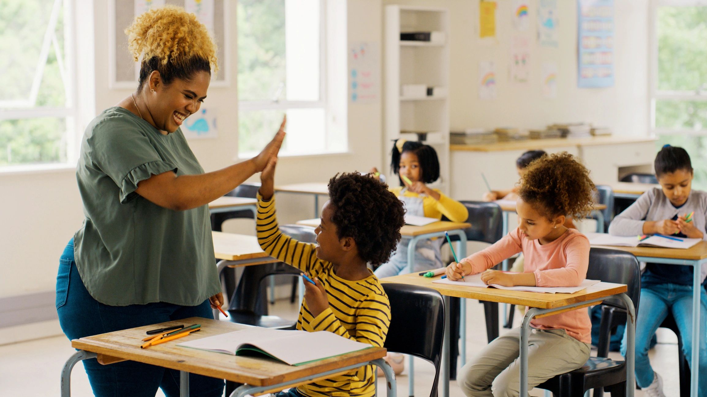 Teacher giving a high-five to a student in a lively classroom.