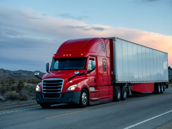 A red semi-truck driving on a highway during sunset.