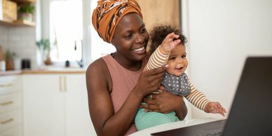 Mother happily holding baby while video chatting on laptop at home.