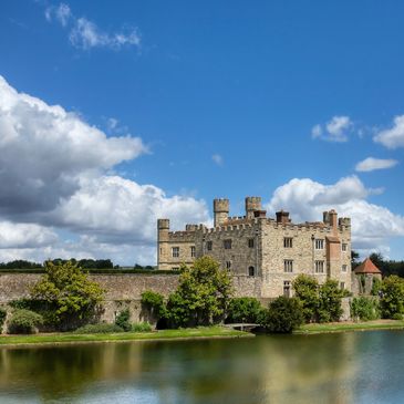 Historic stone castle by a moat under a bright blue sky.