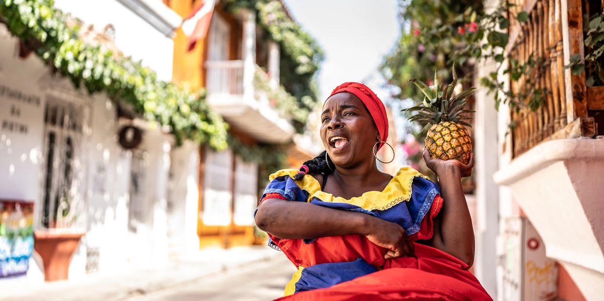 Woman in colorful attire holding a pineapple on a sunny street.