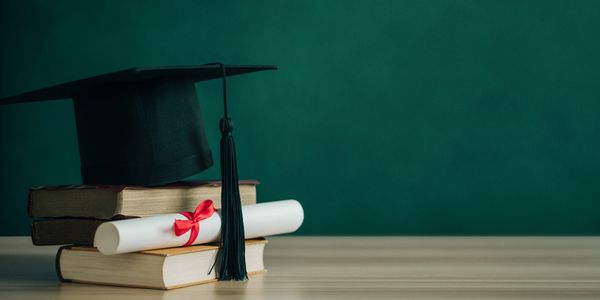 Graduation cap, books, and diploma on table.
