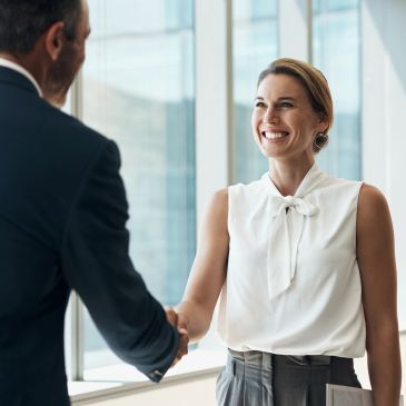Two professionals shaking hands in a bright office setting.