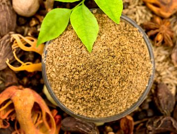 A bowl of ground spices with green leaves on top, surrounded by whole spices.
