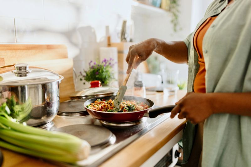 Woman cooking a colourful and nutritious quinoa stir-fry with mixed vegetables and a drizzle of olive oil.