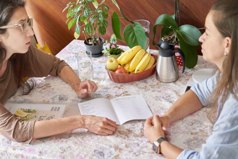 Young nutritionist going over a shopping list of healthy food with a female client at a table in her kitchen during a consultation