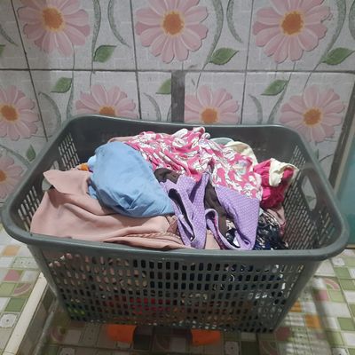 Laundry basket filled with colorful clothes against floral tiled wall.