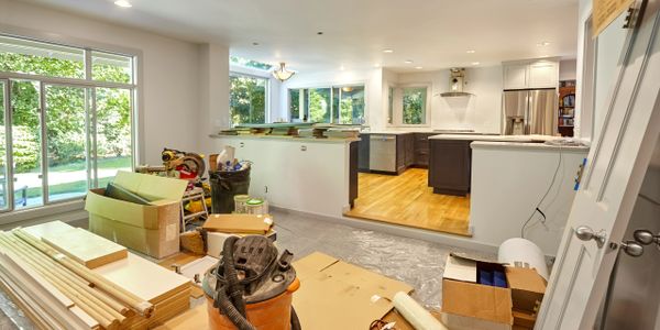Home renovation in progress with construction materials and tools in a bright kitchen and living area.