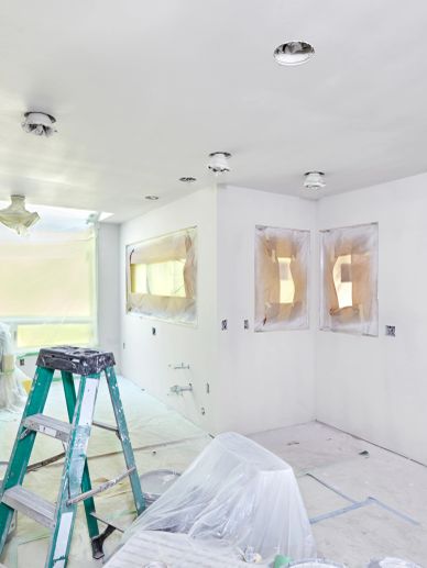 Room undergoing renovation with covered windows and ladder.