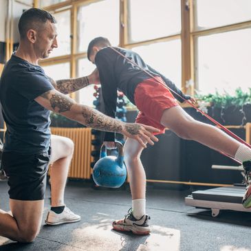 Trainer assists boy with kettlebell exercise in gym.