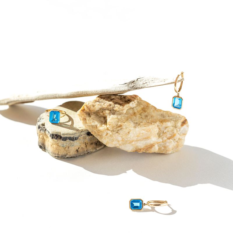 Elegant jewellery set of golden ring andearrings with blue topaz on white background with stones and wood. Minimal style composition with sunlit and shadow. Product still life concept. selective focus