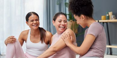Three women laughing and bonding during a relaxing yoga session indoors.