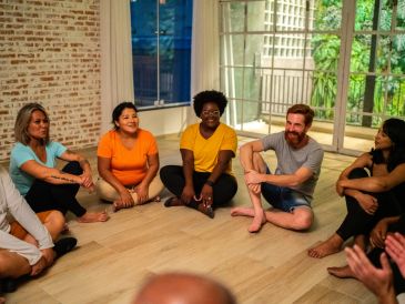 A diverse group sitting barefoot in a circle on a wooden floor indoors.