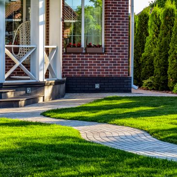 A neat garden path leading to a brick house with green lawn and porch swing.