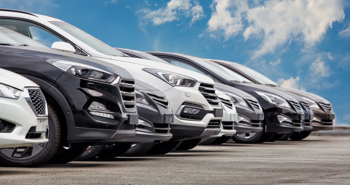 Fila de coches nuevos estacionados bajo un cielo azul.