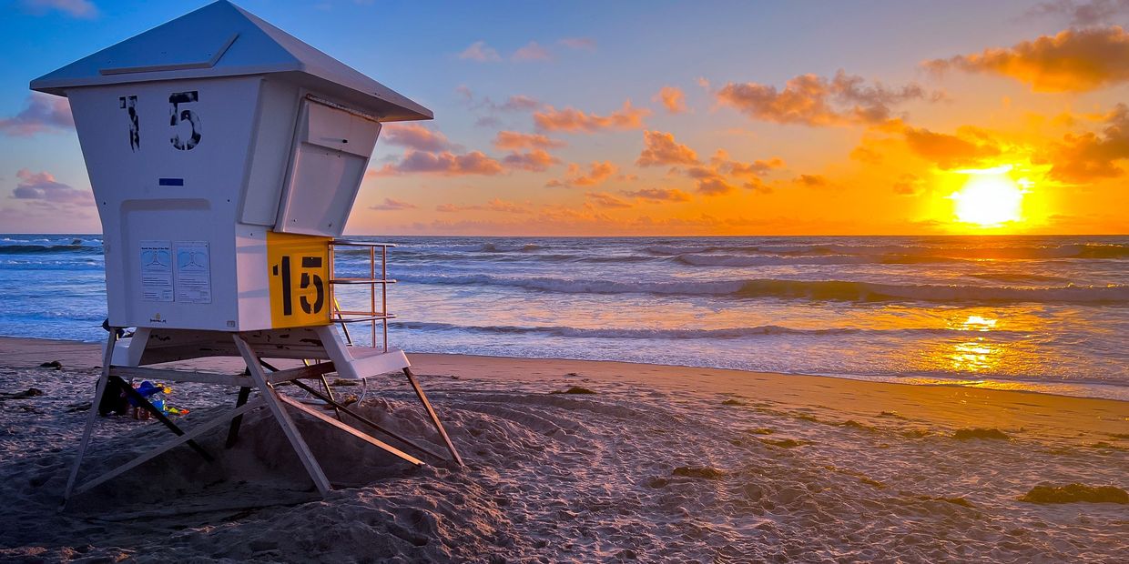 Lifeguard tower 15 on a beach at sunset with colorful sky.