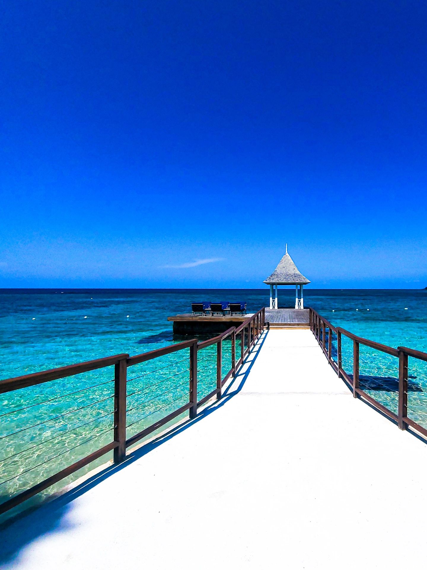 Pier leading to a small gazebo over clear blue water.