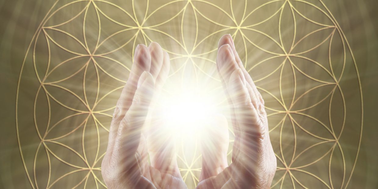 Hands holding a bright light with sacred geometry background.