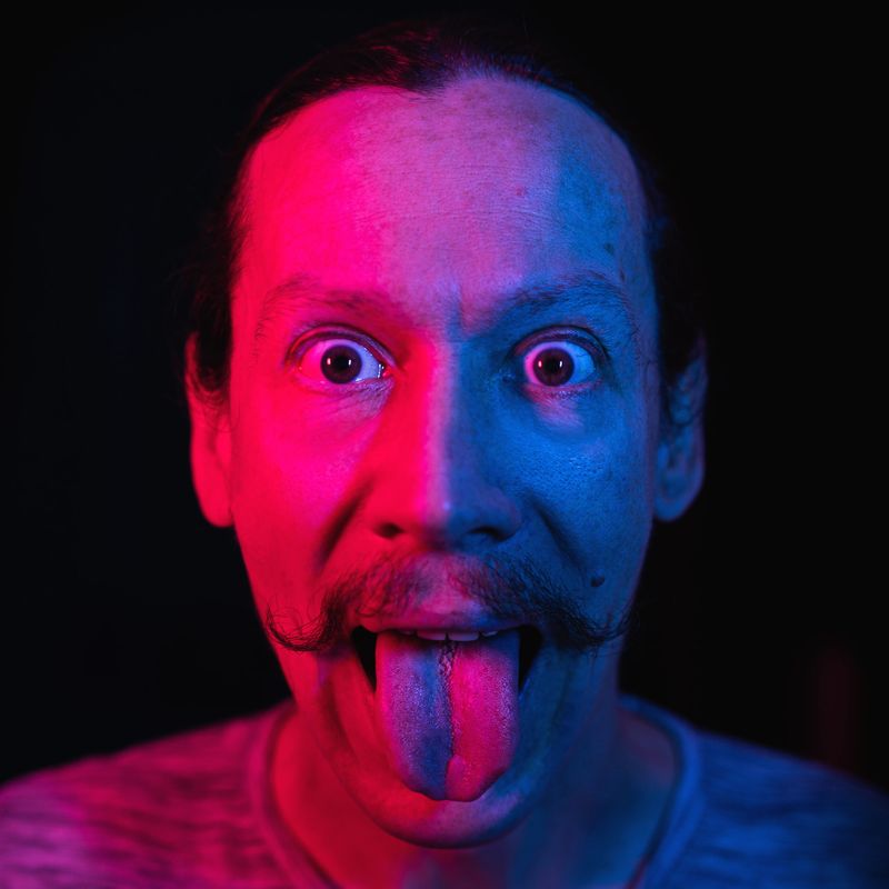 portrait of a man showing tongue in blue-red lighting, emotional art photo