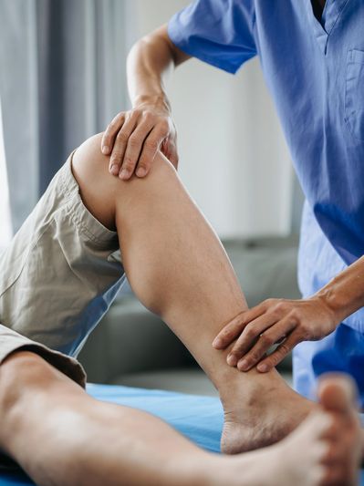 Therapist examining a patient's knee and ankle during a physical therapy session.