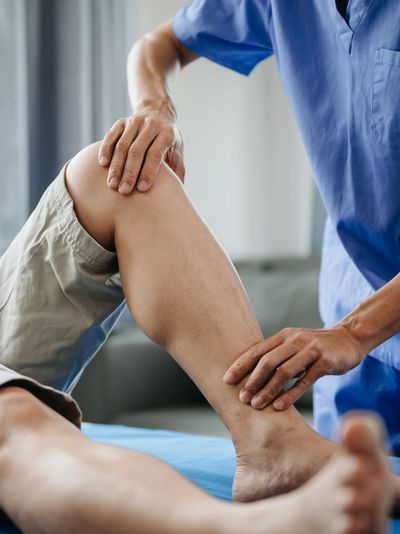 Physical therapist examining a patient's bent knee during rehabilitation.