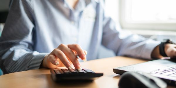 Person using a calculator and laptop at desk.
