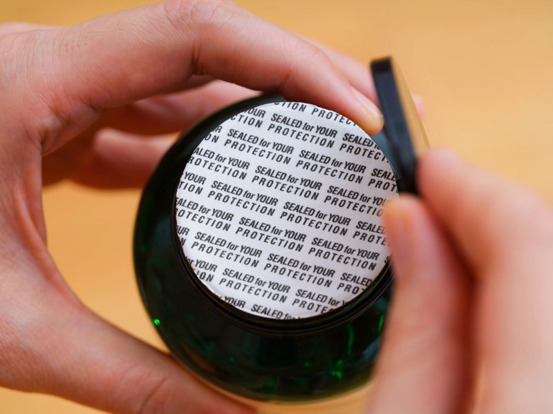 A woman opening a sealed bottle of pills with the world Sealed for Your Protection on it. Close-up.