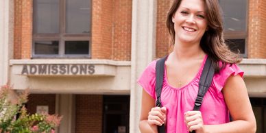 Smiling student with backpack outside admissions office.