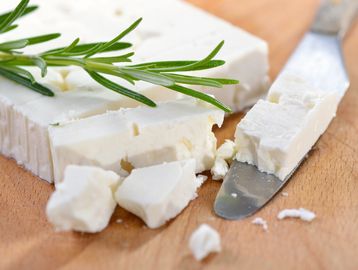 Sliced feta cheese with a sprig of rosemary on a wooden board.