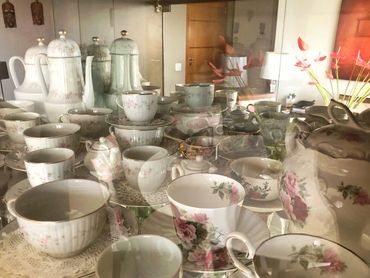 A collection of vintage floral teacups and teapots arranged inside a glass cabinet.
