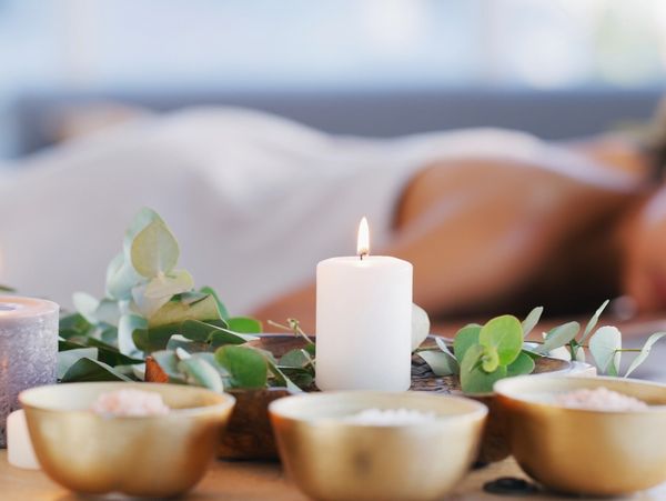 A lit candle and spa bowls with a person relaxing in the background.