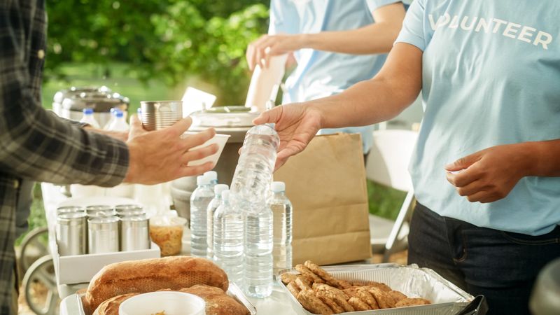 Close Up of an Anonymous Person Handing Over a Water Bottle to Another Person. Green Background in Nature. Outdoors Fourt Court Selling Drinks. Ecology, Healthcare and Hydration Concept.