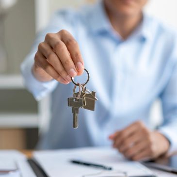Person holding house-shaped keychain with keys.