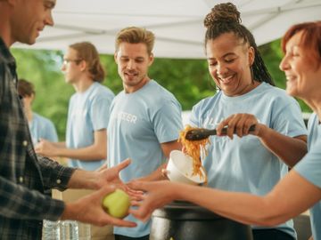Volunteers happily serve food and drinks at an outdoor event.