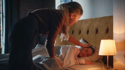 A woman gently touches a sleeping child's forehead in a cozy bedroom.