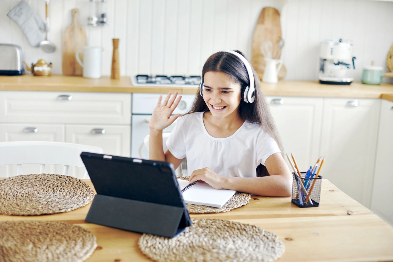 Girl in headphones waving during an online video call at home.