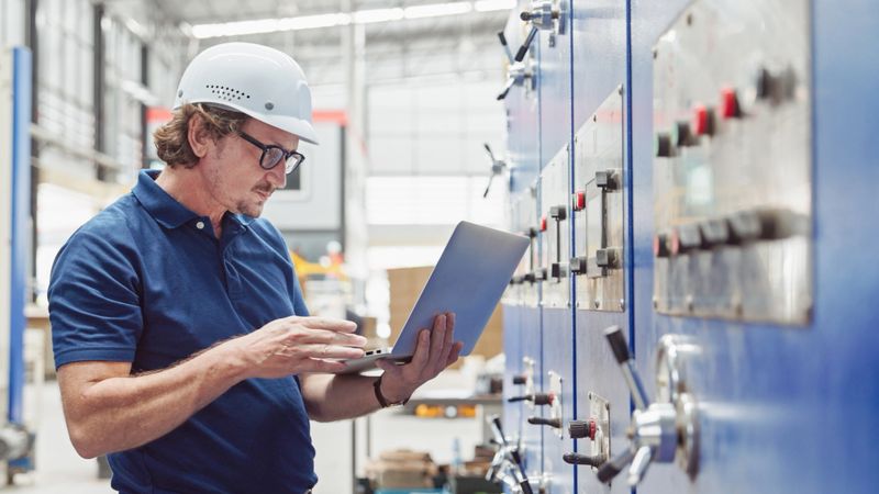 Professional Engineer using a laptop to check quality control, and Manufacturing Operations in front of machinery in the paper packaging factory