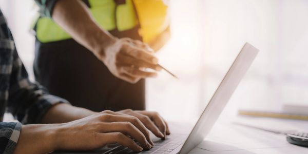 Person typing on laptop with colleague pointing.