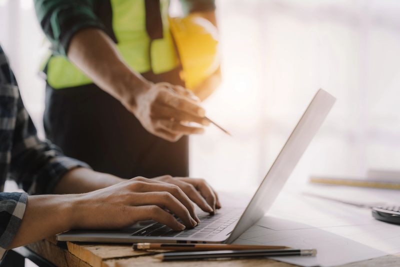 business man hand working and laptop with on on architectural project at construction site at desk in office.