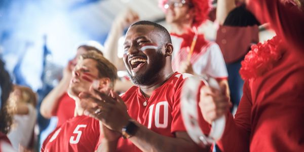 Fans in red jerseys cheer enthusiastically at a sports event.