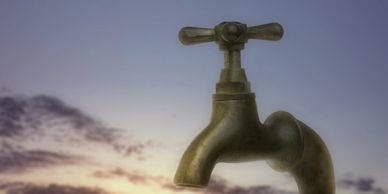 A vintage water faucet against a sunset sky.