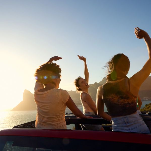 Friends dancing in convertible at sunset.