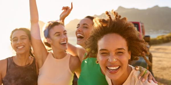 Four women joyfully posing outdoors at sunset with mountains in the background.