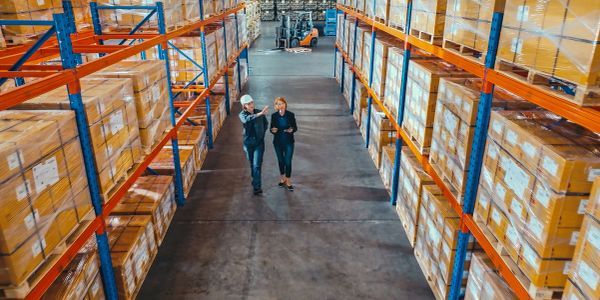 Two workers inspecting a large warehouse filled with boxed goods on shelves.