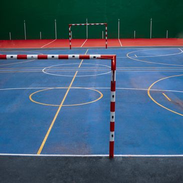 An empty indoor futsal court with blue and red flooring and white goals.