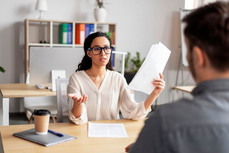 Serious pretty millennial european woman hr manager in glasses with document talk with guy candidate at interview in office interior. Hiring with resume, business in company, recruitment of workers
