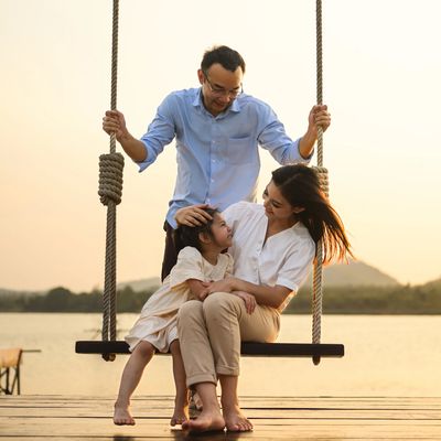 Family enjoying a moment on a swing by the water at sunset.