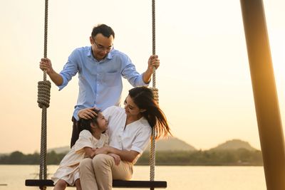 Happy family enjoying a swing at sunset outdoors.