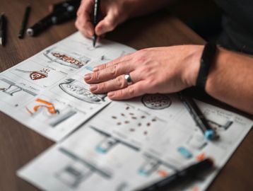 Person sketching designs on paper with markers.