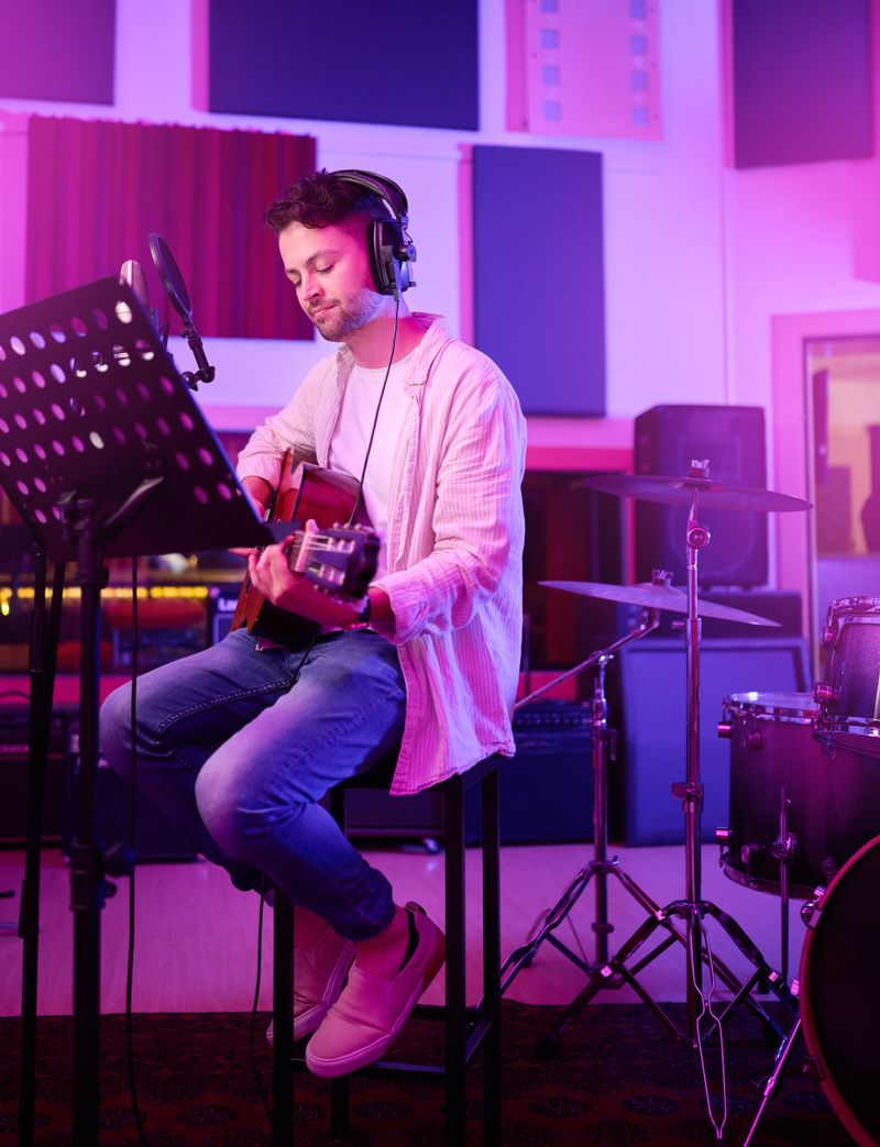 Musician, headphones or guitar in neon studio, recording production or performance on radio mic, label or band concert. Guitarist, artist or man playing on strings instrument in night light practice